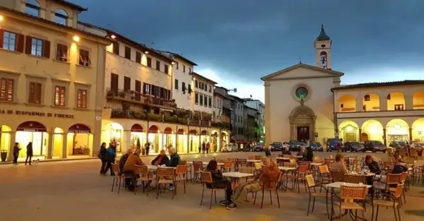 Piazza serale con tavolini all'aperto e una chiesa, un'atmosfera incantevole nei borghi da visitare vicino a Figline Valdarno.