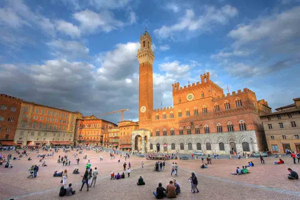 Piazza del Campo a Siena, un luogo iconico per il turismo, con il Palazzo Pubblico e la Torre del Mangia sotto un cielo nuvoloso.