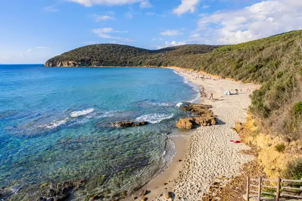 Spiaggia delle Bandite di Scarlino con acque cristalline, sabbia dorata e vegetazione rigogliosa. Persone rilassate al sole.